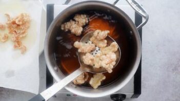 A slotted spoon holding fried pork rinds over a fry bath.