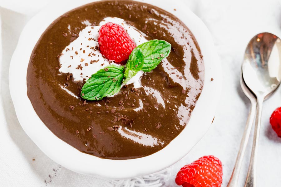 creamy, thick chocolate pudding with raspberries, whipped cream and mint next to two spoons