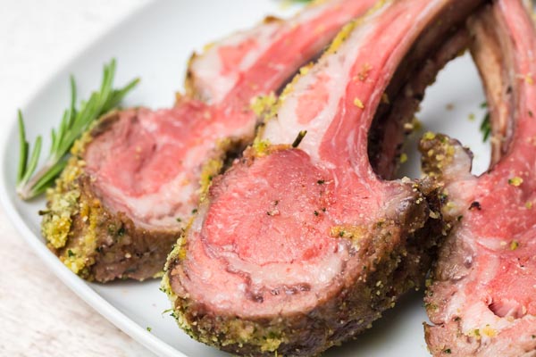 medium rare rack of lamb on a plate with a sprig of rosemary