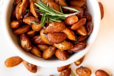 a white bowl with a bunch of seasoned almonds in it topped with rosemary