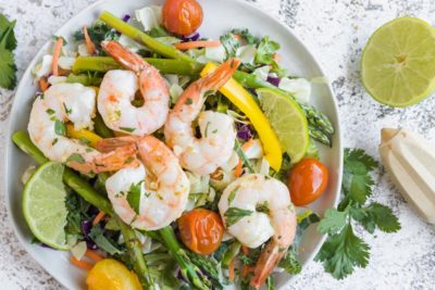 shrimp on top of a salad with bursting tomatoes and cilantro