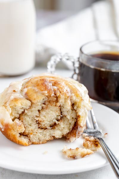 Half eaten cinnamon roll on a plate with gooey layers of butter cinnamon in the center.