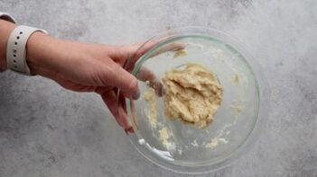 A hand holding a glass bowl with bread dough inside.