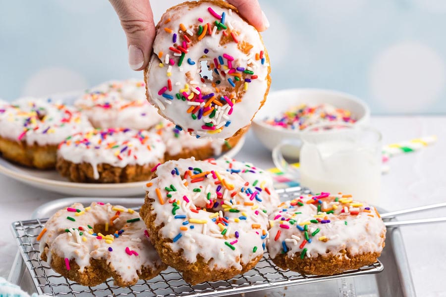 A hand holding a glazed donut over a wire rack filled with more donuts.