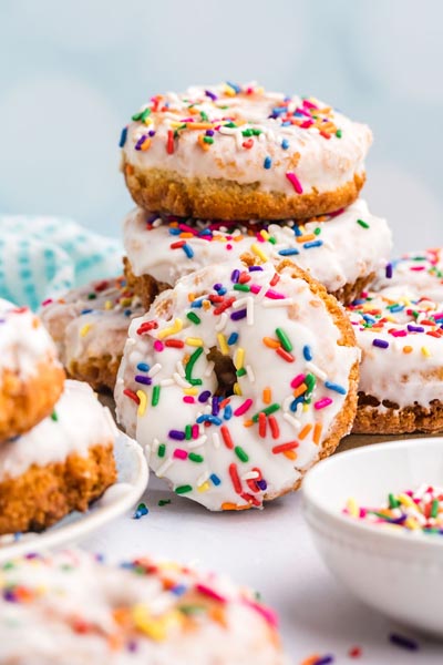 A stack of glazed donuts covered with colorful rainbow sprinkles.