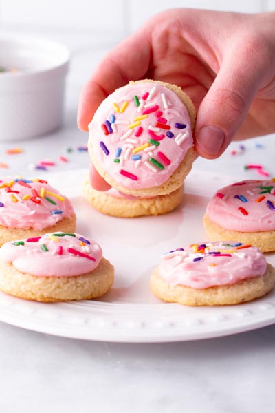 A hand holding a frosted cookie over a plate of cookies.