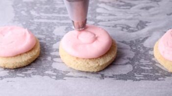 Piping a swirl of pink frosting on a round sugar cookie.