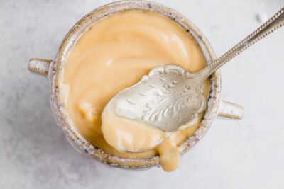 Looking down into a small earthen bowl with creamy sweetened condensed milk inside. An old rustic spoon lays on top the bowl.