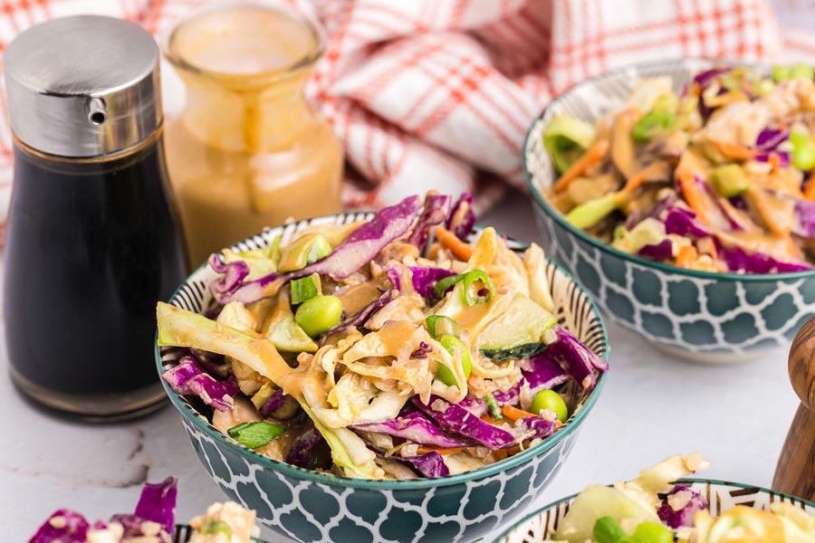 Two bowls of thai chicken salad in front of soy sauce and peanut dressing.