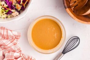 A bowl with creamy peanut dressing next to a whisk.