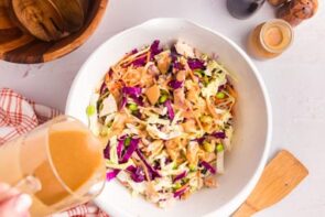 Pouring peanut dressing onto a bowl with crunchy thai salad.