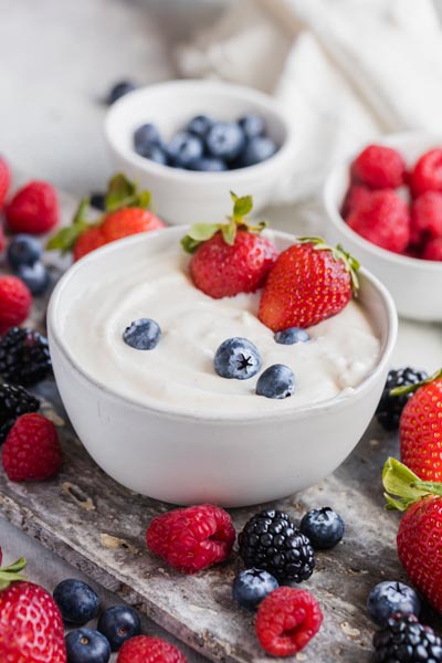 A bowl of dip topped with fruit and mixed berries in bowls and on the platter.